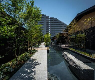 Long reflecting pool with stone feature beside a wooden ryokan building and landscaped trees in Kyoto setting