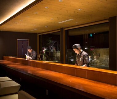 Long wooden counter with chefs preparing dishes at HOSHINO-OTOー星音 ryokan in Kyoto