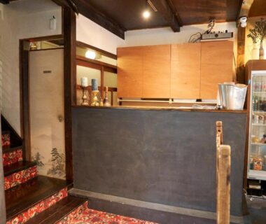 Low wooden reception counter with carpeted stairs and small display fridge at HOTEL Clam Chowder in Kyoto