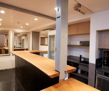 Long wooden counters and kitchenette in HOTEL Clam Chowder interior with modern lighting, Kyoto ryokan setting