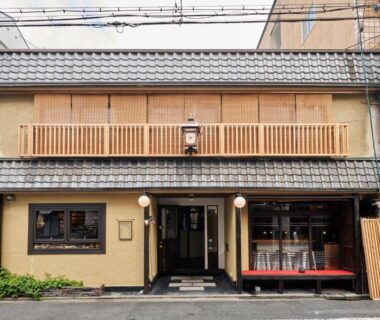 Two-story ryokan facade with wooden balcony, lantern and street entrance in Kyoto, Kansai