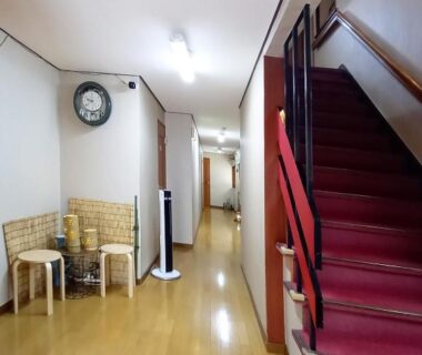 Corridor with wooden floor, red-carpeted stairs and wicker seating at HOTEL HOUSE LEE in Tokyo