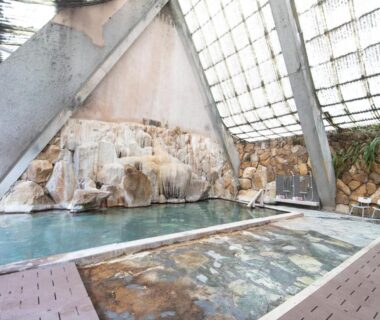 Indoor onsen baths with rock wall and wooden decking at HOTEL SHIRAHAMAKAN Wakayama