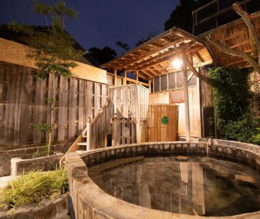 Round stone onsen bath beside wooden fence and lantern-lit entrance at HOTEL SHIRAHAMAKAN Wakayama