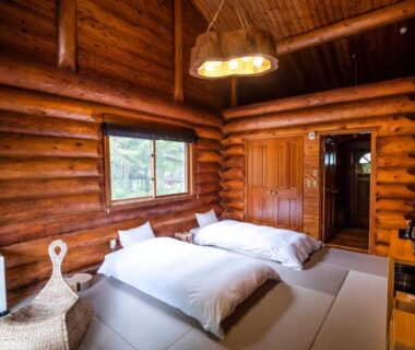 Log cabin room with tatami floor, two low futon beds, exposed wooden logs and window at Hacho no Yu, Tochigi
