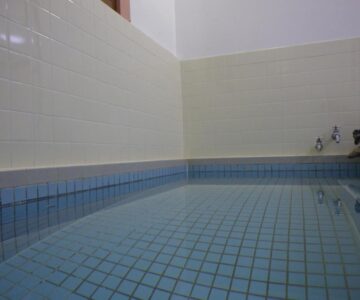 Indoor blue-tiled bath with wall-mounted faucets and high tiled walls at Hagurokan Yamagata