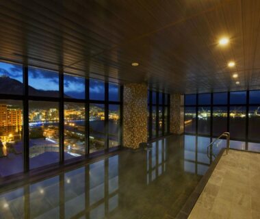 Indoor onsen pool with floor-to-ceiling windows overlooking city lights and mountains at Hakodate Kokusai Hotel Hokkaido