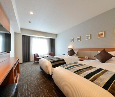 Twin beds with striped runners, seating area, wall art and desk at Hakodate Kokusai Hotel in Hokkaidō