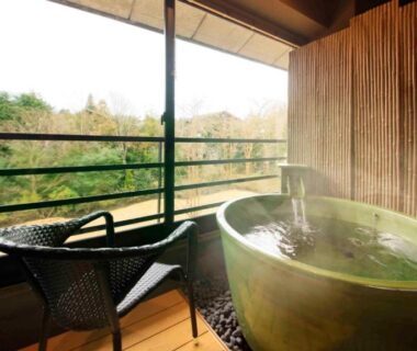 Wooden balcony with green ceramic onsen tub, two chairs and forested mountain view at Hakone Fuga, Kanagawa