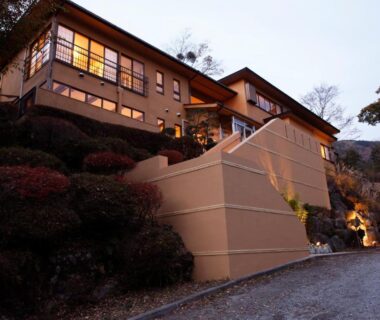 Exterior of Hakone Fura on hillside with illuminated windows, stone steps and landscaped shrubs in Kanagawa