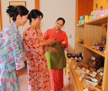 Three guests in yukata examining souvenirs on wooden shelves inside a ryokan shop at Hakone Hoshi no Akari, Kanagawa