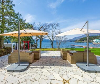 Stone patio with loungers and umbrellas overlooking lake and distant hills at Hakone Hotel, Kanagawa