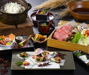 Traditional multi-course Japanese meal with sashimi, rice pot, and hot pot ingredients arranged on trays