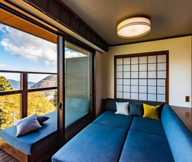 Tatami room with low sofa, shoji screens and floor-to-ceiling window overlooking forested hillside