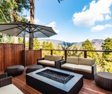 Wooden terrace with sofa seating, umbrella and central fire table overlooking forested hills in Kanagawa