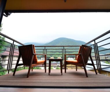 Balcony with two wooden chairs and table overlooking forested hills at Hakone Onsen Ryokan Yaeikan, Kanagawa