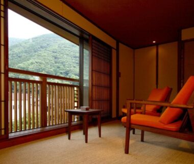 Tatami room with two armchairs, shoji screens and balcony overlooking wooded hills at Hakone Onsen Ryokan Yaeikan, Kanagawa