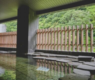Covered onsen bath with stone stepping path, wooden fence and lush hillside backdrop at Hakone Pax Yoshino