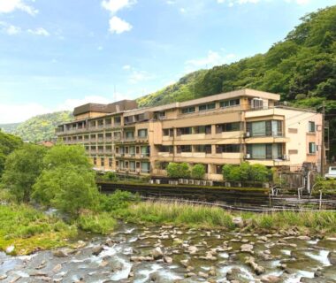 Riverfront exterior of Hakone Pax Yoshino ryokan with forested hills in Kanagawa