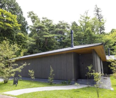 Single-story wooden villa with pitched roof, chimney, lawn and surrounding trees in Kanagawa
