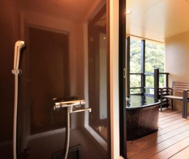 Indoor shower and wooden soaking tub opening to balcony with chairs and greenery, Hakone Suimeisou, Kanagawa