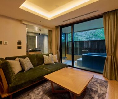 Sofa and table facing sliding doors to a wooden outdoor soaking tub and small garden