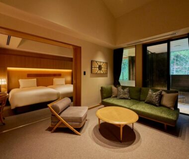 Guest room with bed, green sofa, round table and garden-facing sliding doors at Hakone Suishoen in Kanagawa