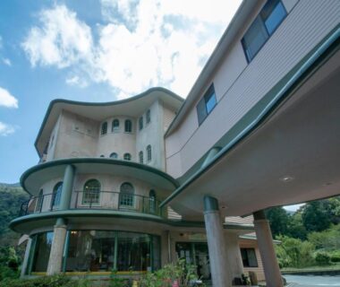 Multi-story curved facade with balconies at Hakonenomori Okada in Kanagawa against a mountain backdrop