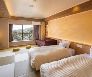 Bright tatami room with two beds, low seating, cushions, and window overlooking wooded hills