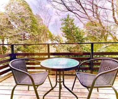Wooden deck with round glass table and two chairs overlooking trees at Hakonesaryo Kintoki Kanagawa