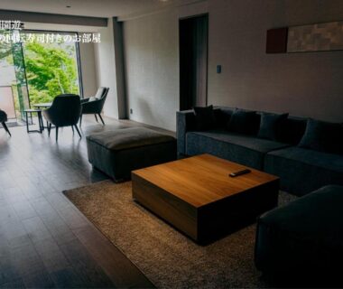 Spacious lounge with sectional sofa, low wooden coffee table and floor to ceiling window opening to balcony and greenery