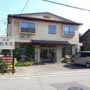 Two-story ryokan exterior with entrance, signage and parked car on street in Hakuraiso, Nagano, Chūbu
