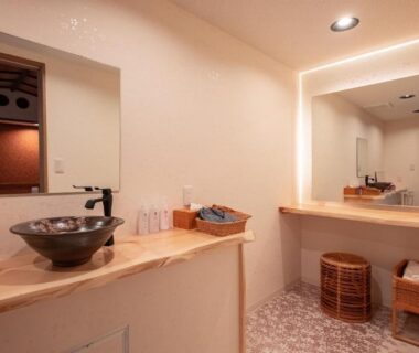 Spacious washbasin area with wooden counter, mirror and wicker stools at Hakuunsou Kanagawa