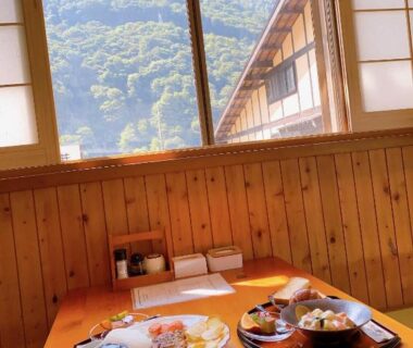 Low wooden dining table with meal trays beside shoji windows overlooking forested Gifu mountains at Hakuunsou