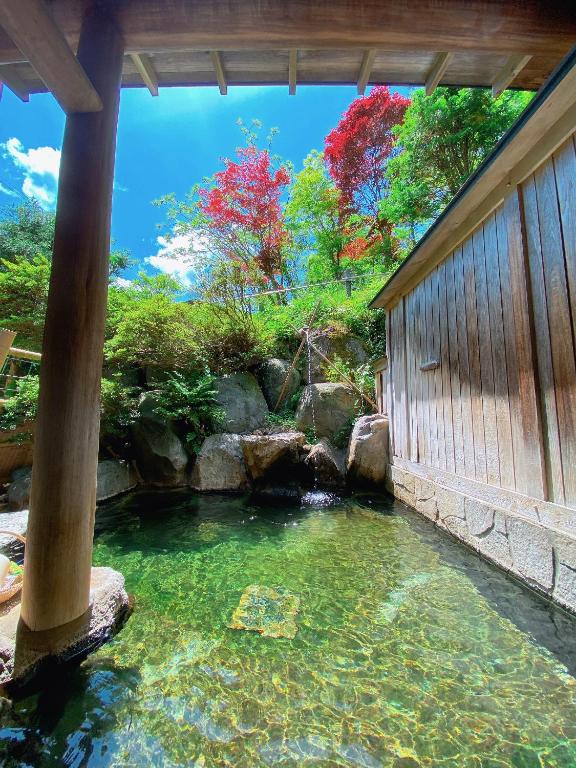 Outdoor Onsen Hakuunsou Gifu Japan Clear outdoor bath with stone edge, wooden fence and red-leaf trees at Hakuunsou in Gifu