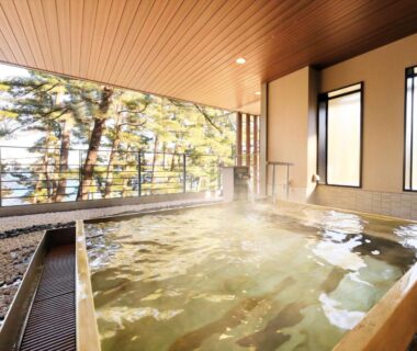 Steaming indoor wooden onsen bath with large windows overlooking pine trees at Hamabeno Ryouriyado Houraikan in Iwate Tōhoku