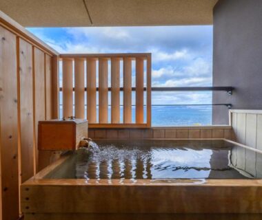 Wooden soaking tub with sea view through slatted screen at Hamachidorinoyu Kaisyu in Wakayama