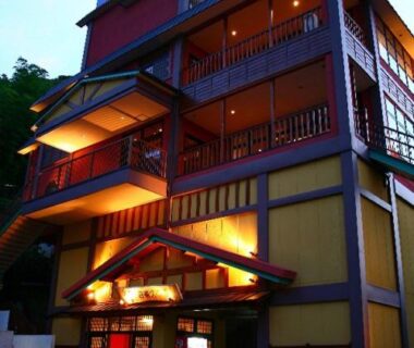 Multi-story ryokan exterior with lit wooden balconies and entrance at dusk in Kumamoto, Kyushu