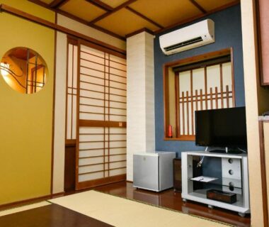 Tatami room with shoji screens, television, air conditioner and low wooden furnishings at Hamazen Ryokan, Kumamoto