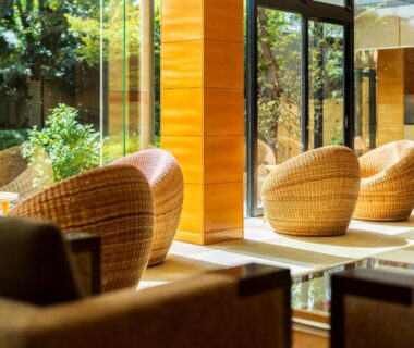 Glass-front lounge with woven chairs and garden view at Hana Beppu in Ōita, Kyūshū
