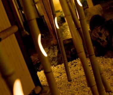 Warm-lit bamboo poles lining a gravel walkway at a ryokan entrance in Beppu, Ōita