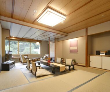 Spacious tatami room with low table, floor cushions, large window and wooden ceiling at HanaMOMIJI in Hokkaidō