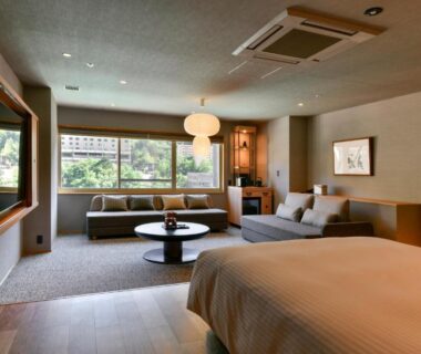 Bright guest room with bed, sofa, low table and large window overlooking lush greenery