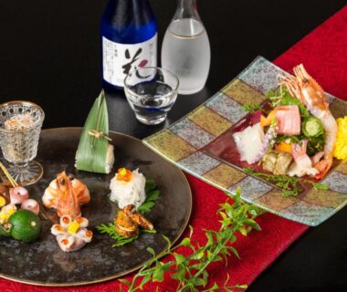 Plates of assorted seafood and garnishes with sake carafe and cup on red runner at Hanabishi Hotel Hokkaidō