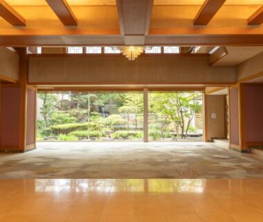 Lobby with floor-to-ceiling windows opening to a manicured garden, wooden beams and warm lighting at Hanabishi Hotel