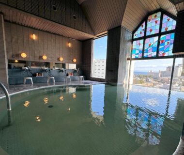 Spacious indoor bath with stained glass window and city view at Hanabishi Hotel Hokkaidō