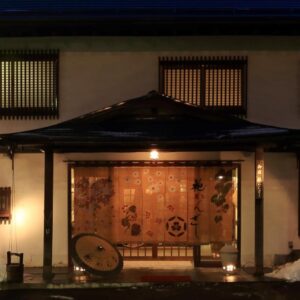 Entrance with noren curtain, lantern glow and snow at Hanakanzashi ryokan in Fukushima