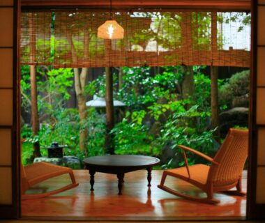 Wooden alcove with low round table, two lounge chairs and lush garden framed by shoji and bamboo blinds