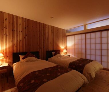 Warmly lit twin beds with shoji screens and wooden paneling at Hanakanzashi ryokan Fukushima