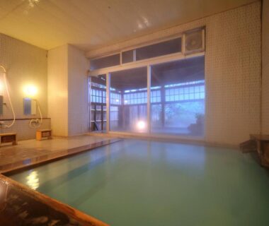 Tiled indoor onsen with wooden edge, wash stations and large frosted window at Hanakanzashi in Fukushima